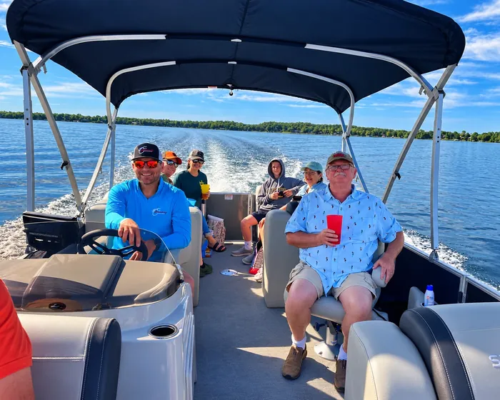 Brady Baxter at the wheel of the Sylvan pontoon with a family group aboard on a sunny afternoon