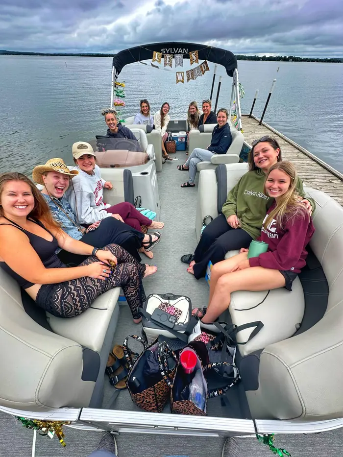 A bachelorette group under a Let's Go Wild banner aboard the Baxstar Outdoors Sylvan pontoon at the dock