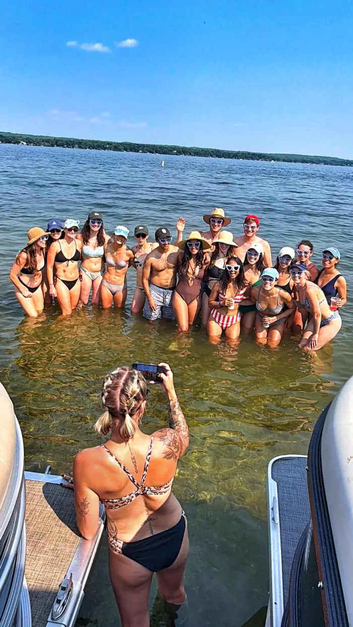 A large group posing in shallow water at the sandbar beside the pontoon