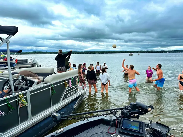 Cruise guests playing volleyball in the shallow water at the sandbar beside the decorated pontoon